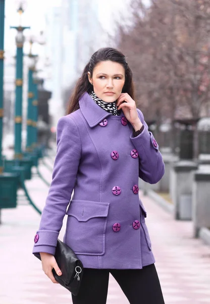 Bella ragazza in un cappotto nel parco con una frizione in mano — Foto Stock