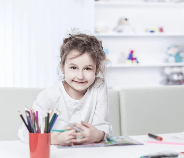 Vijf jaar oud meisje tekent met krijtjes zittend aan tafel in de kinderkamer — Stockfoto