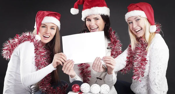 Três meninas no traje de Papai Noel mostrando folha em branco — Fotografia de Stock