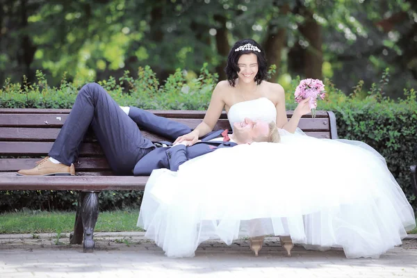 Bruden och brudgummen vilar på en bänk — Stockfoto