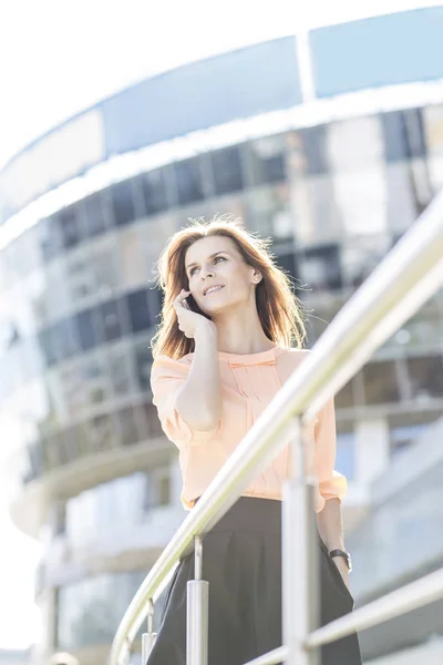 Mulher de negócios de sucesso falando no smartphone na frente de um grande edifício de escritórios moderno — Fotografia de Stock