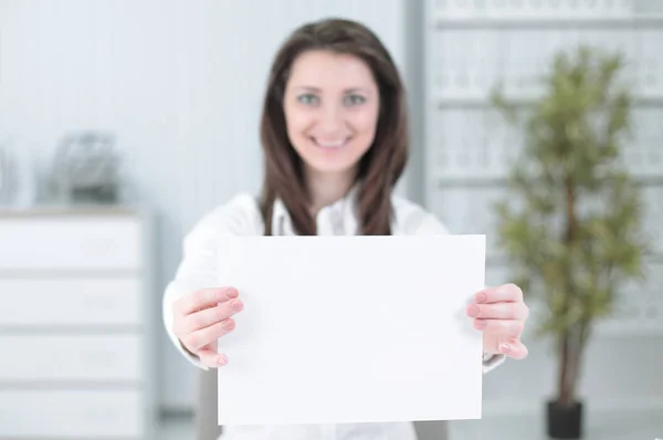 Business kvinna visar tomt ark, sitter bakom ett skrivbord — Stockfoto