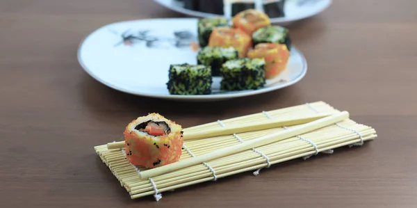 Rolos de sushi e pauzinhos em uma mesa de madeira — Fotografia de Stock