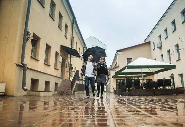 Feliz pareja amorosa está bajo un paraguas en una calle de la ciudad en un día lluvioso — Foto de Stock