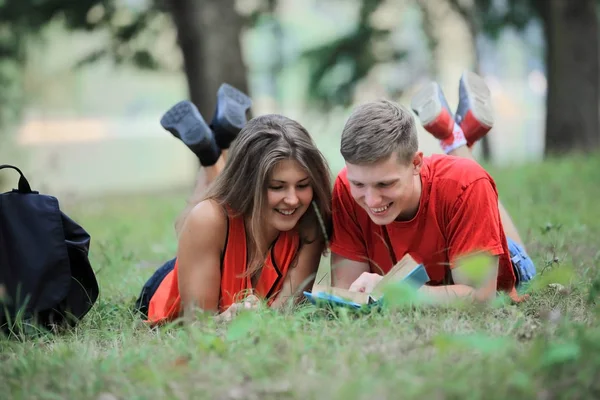 Pareja de estudiantes tumbados en la hierba del parque y leyendo un libro —  Fotos de Stock
