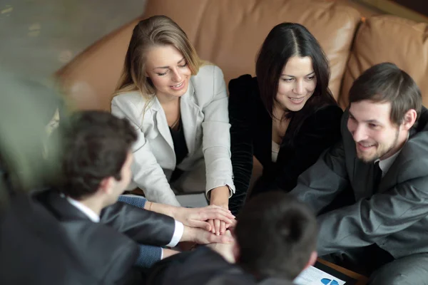Groep van tevreden zakelijke mensen hand in hand samen zittend rond het Bureau — Stockfoto