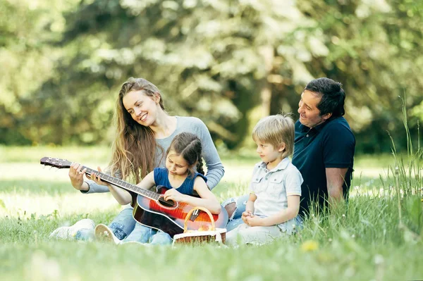 Happy family with a guitar, sitting on the lawn in the Park — Stock Photo, Image