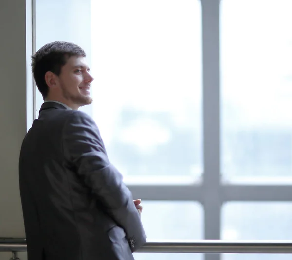 Sonriente hombre de negocios de pie cerca de una gran ventana de oficina — Foto de Stock