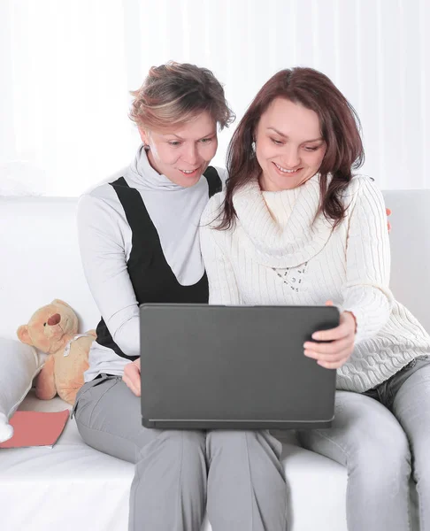 Mutter und Großmutter schauen auf den Laptop-Bildschirm, der auf der Couch im Kinderzimmer sitzt — Stockfoto