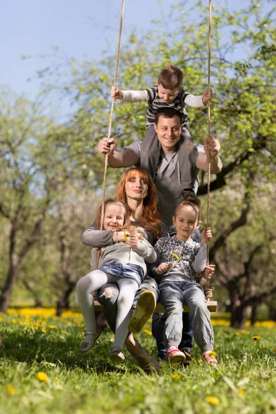 Amistosa y alegre familia en un columpio en el Parque —  Fotos de Stock