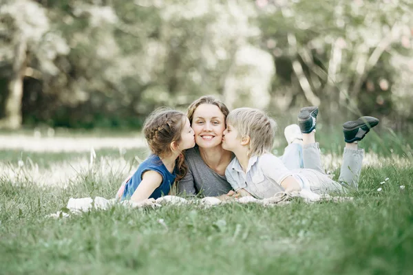Брат и сестра целуют маму на лужайке в парке — стоковое фото