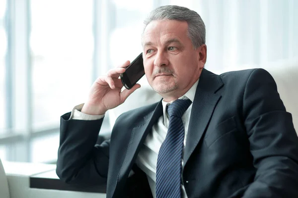 Mature businessman talking on mobile phone in office — Stock Photo, Image