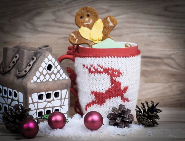 Weihnachtstasse und ein Lebkuchenhaus und Weihnachtskugeln auf einem Tisch — Stockfoto