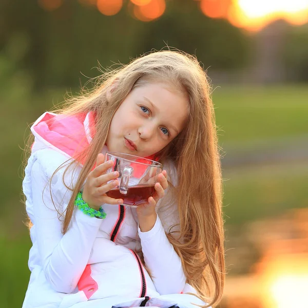 Linda niña con una taza de té sentado en un banco en el coo — Foto de Stock