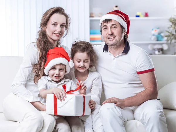 Met de gift van Kerstmis zittend op een bank in de kinderkamer en gelukkige familie. — Stockfoto