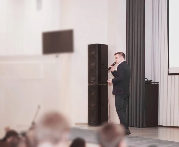 Спикер ведет бизнес конференции стоя перед большим белым экраном на сцене в конференц-зале — стоковое фото