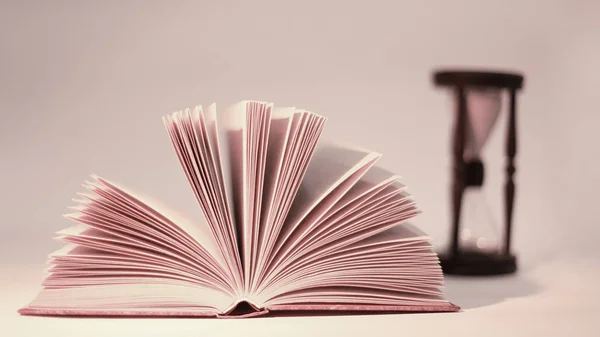 Libro abierto y reloj de arena. aislado sobre fondo amarillo en colores cálidos — Foto de Stock