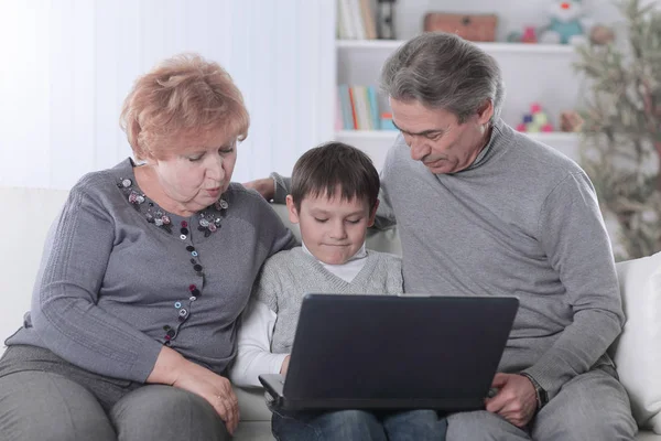 Abuela, abuelo y nieto mirando la pantalla del ordenador portátil mientras se relaja en el sofá —  Fotos de Stock