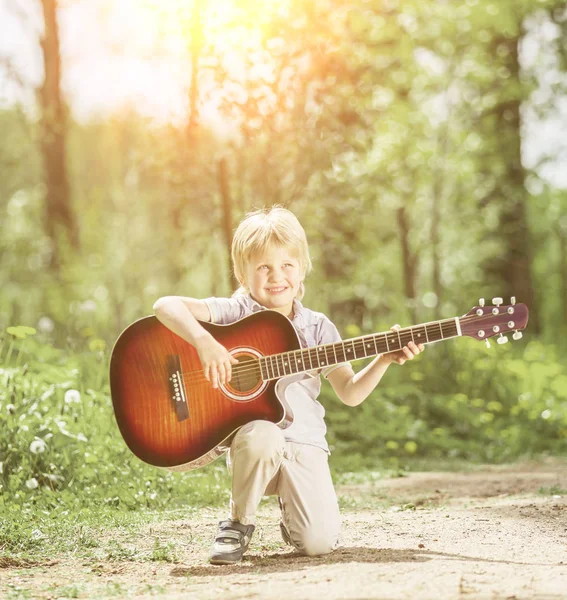 Mały chłopiec z gitarą w parku lato — Zdjęcie stockowe