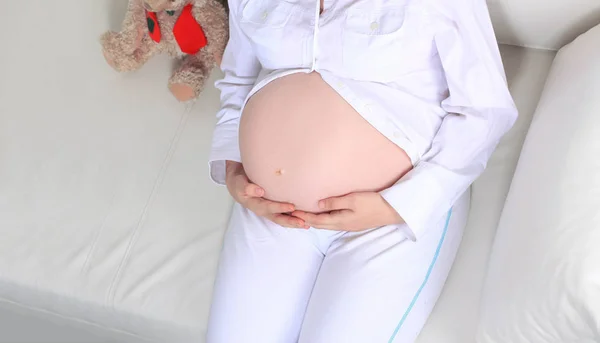 Nahaufnahme. Schöne schwangere Frau mit einem Stofftier auf der Couch liegend. — Stockfoto