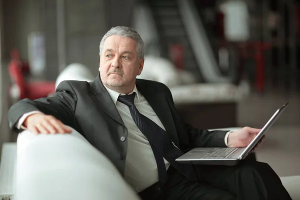 Pensive businessman with laptop sitting in office lobby — Stock Photo, Image