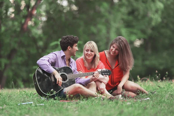 Grupo de estudantes com uma guitarra relaxar sentado na grama no parque da cidade — Fotografia de Stock