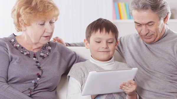 Abuela, abuelo y nieto mirando la tableta digital mientras se relaja en el sofá —  Fotos de Stock