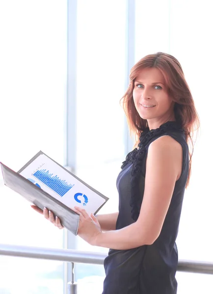 Moderne Geschäftsfrau mit Finanzkarten, während sie in der Nähe eines großen Bürofensters steht — Stockfoto