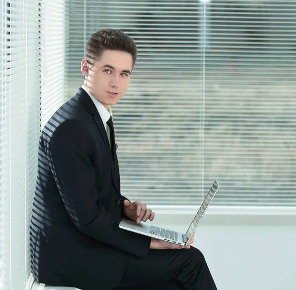 Jovem empregado trabalhando em um laptop sentado no corredor do th — Fotografia de Stock