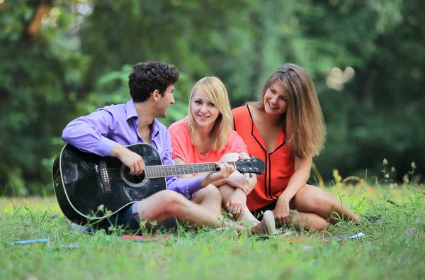 Grupo de estudantes com uma guitarra relaxar sentado na grama no parque da cidade — Fotografia de Stock