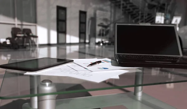 Laptop e documentos financeiros em uma mesa em um escritório espaçoso — Fotografia de Stock