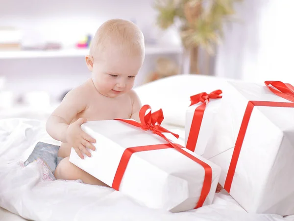 Pretty baby plays with gift boxes sitting on the couch — Stock Photo, Image