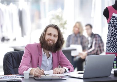 modern bir stüdyoda masada gülümseyen moda tasarımcısı.