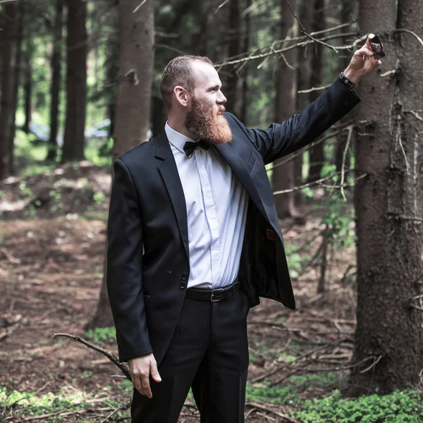 Allvarlig man i kostym tar en selfie i en skog. — Stockfoto