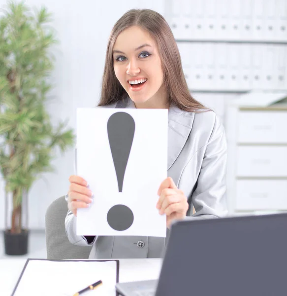 Mujer de negocios sosteniendo el signo de exclamación, sentado detrás de un escritorio — Foto de Stock