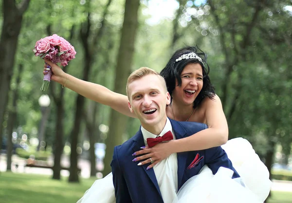 Marié porte sa mariée sur le dos dans le parc . — Photo