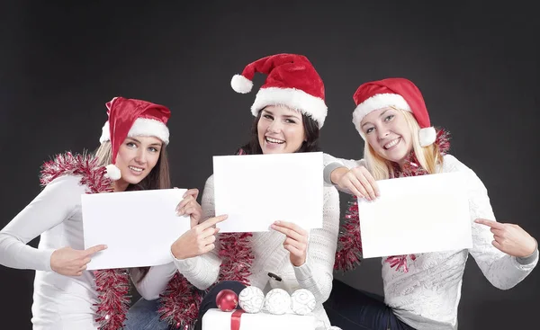 Três meninas no traje de Papai Noel mostrando folha em branco — Fotografia de Stock