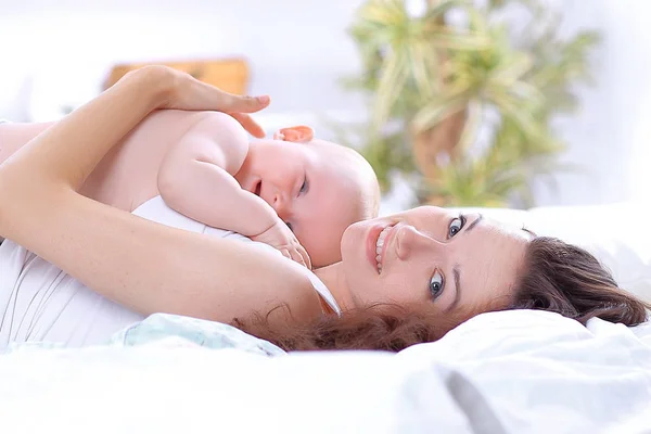 Jonge moeder speelt met de baby liggend op het bed — Stockfoto