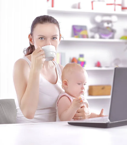 Joven mamá con pequeño bebé sentado en el Desk.the concepto de freelancing — Foto de Stock