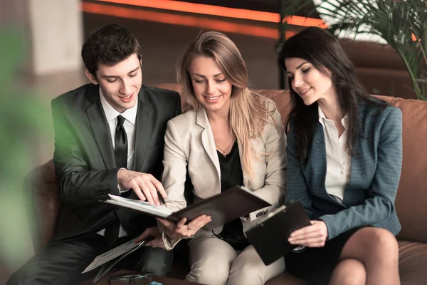 Equipe de negócios discutindo documentos de trabalho sentados no sofá no lobby de um escritório moderno — Fotografia de Stock