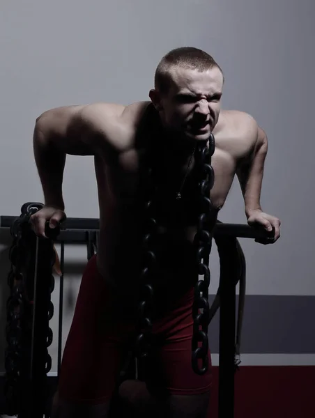 Fisiculturista masculino elegante com uma cadeia pesada em pé no ginásio . — Fotografia de Stock