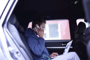 bir dizüstü bilgisayar ve cep telefonu arabada oturan iş adamı kullanır