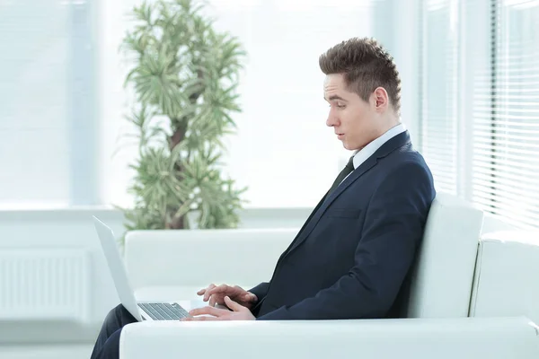 Schöner Geschäftsmann tippt auf Laptop sitzt in der Lobby des th — Stockfoto