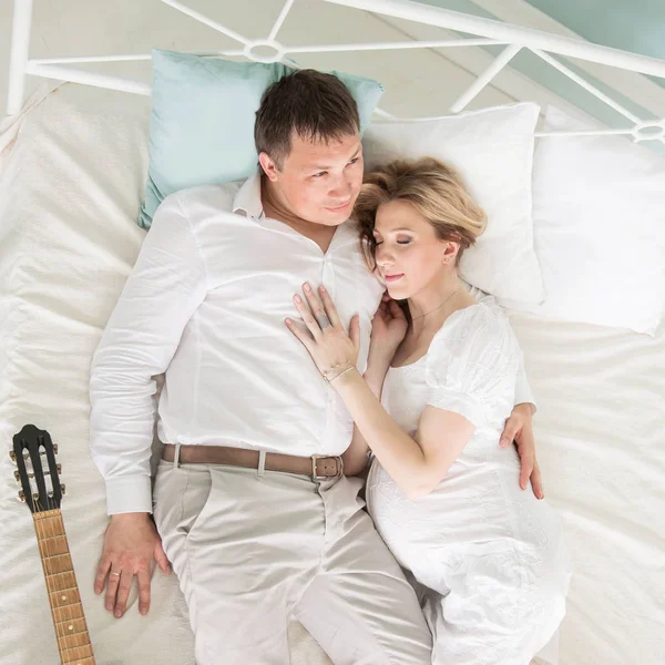 Cariñoso marido con una guitarra y su esposa embarazada en la cama en — Foto de Stock