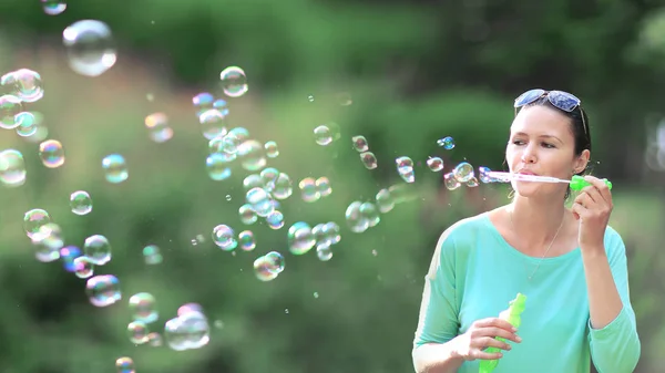 Gorgeous young brunette girl blowing soap bubbles in sunlit park. — Stock Photo, Image