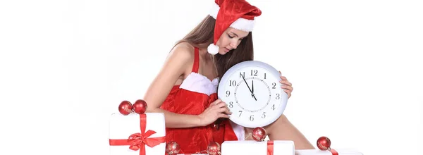 Smuk ung kvinde i juledragt med et ur sidder på kasserne med julegaver. - Stock-foto