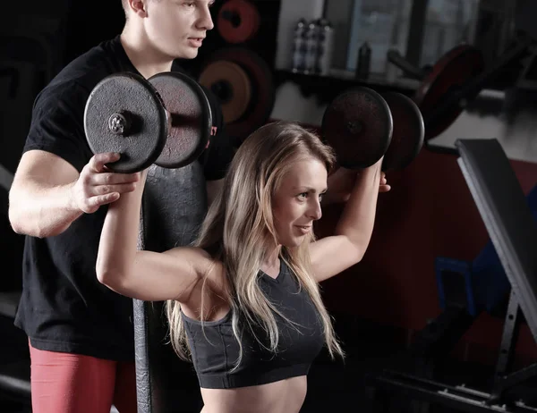 Jovem com personal trainer exercitando-se no simulador no ginásio — Fotografia de Stock