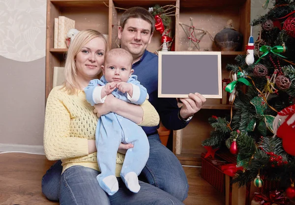 Padres felices jóvenes mostrando tarjeta de Navidad en blanco — Foto de Stock