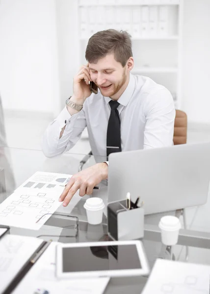 Uśmiechający się biznesmen rozmawia przez telefon, siedząc przy biurku — Zdjęcie stockowe