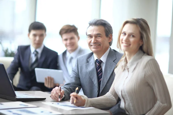 Porträt eines reifen Geschäftsmannes, der bei einem Treffen mit Kollegen im Hintergrund lächelt — Stockfoto